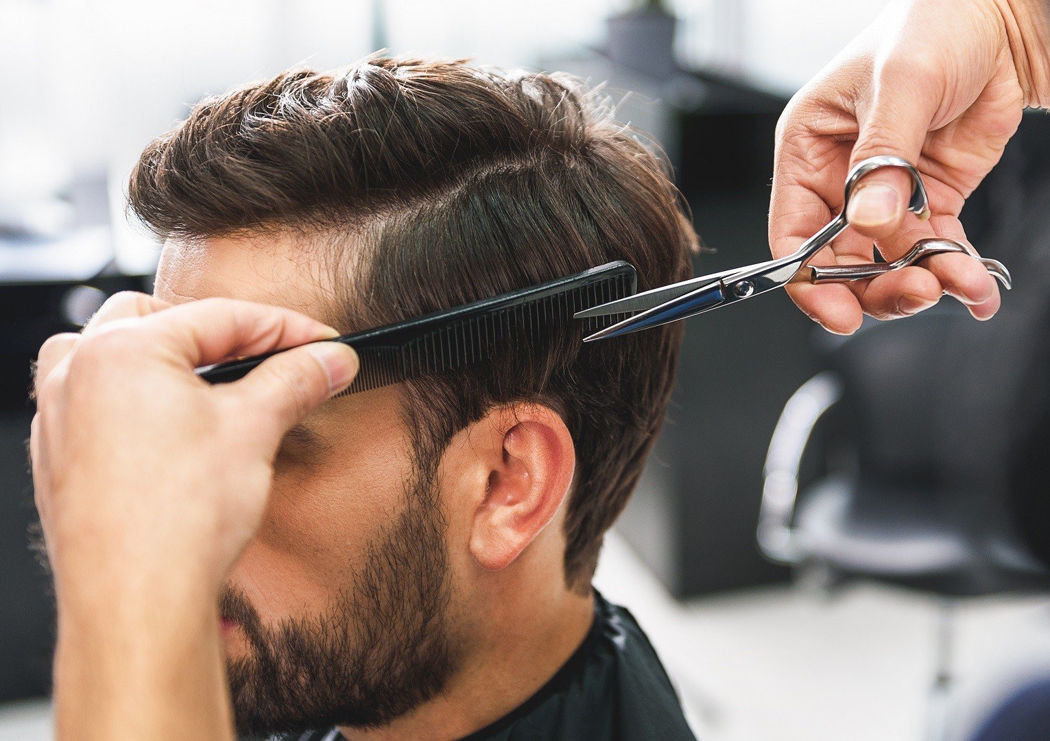 Close up of hairdresser arms cutting and combing male hair